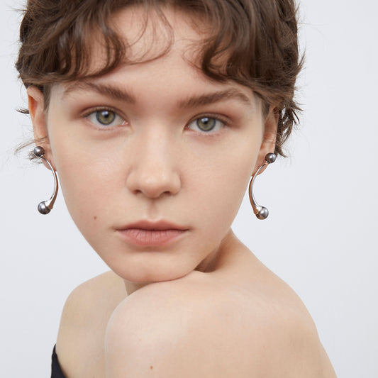 Front view of a model wearing TIKOO modern curved grey pearl earrings with a wave-patterned necklace.