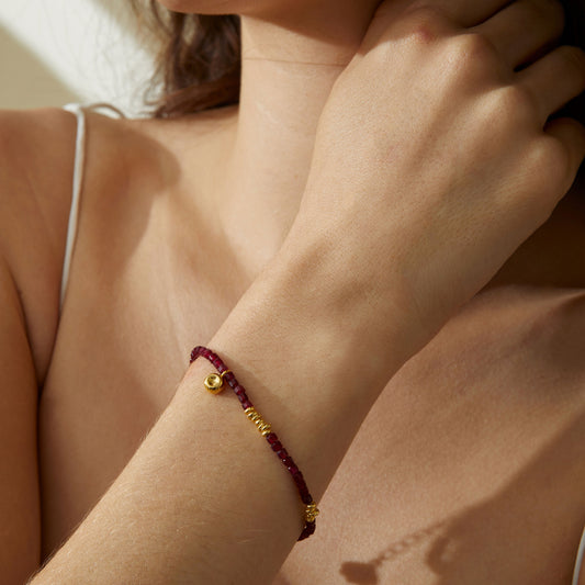 Close up of a model wearing TIKOO red garnet bead bracelet, showcasing the 18K gold accents and vibrant red stones.