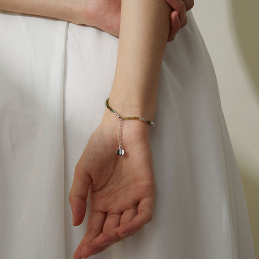 Close up of a model wearing TIKOO tourmaline gemstone bracelet with a white summer dress, boho-chic jewelry styling.