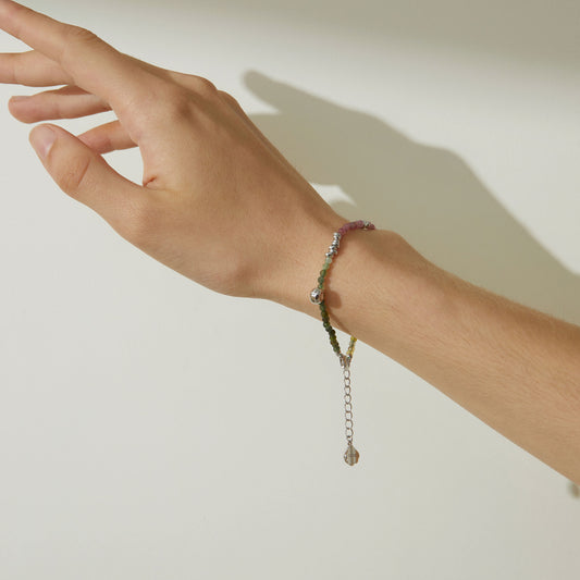 Close up of a model wearing TIKOO tourmaline gemstone bracelet with a white summer dress, boho-chic jewelry styling.