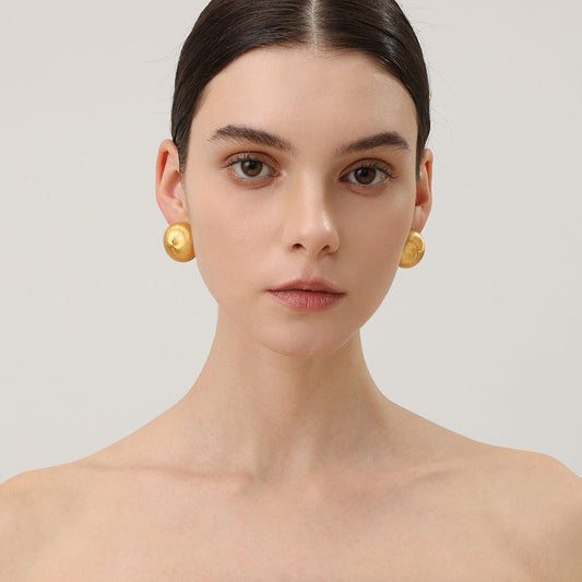 Close-up of TIKOO handcrafted original design brushed gold earrings showing texture.