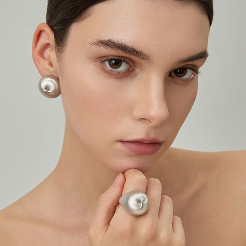 Close-up of a model wearing TIKOO large organic domed stud earrings and matching ring for a modern fashion look.
