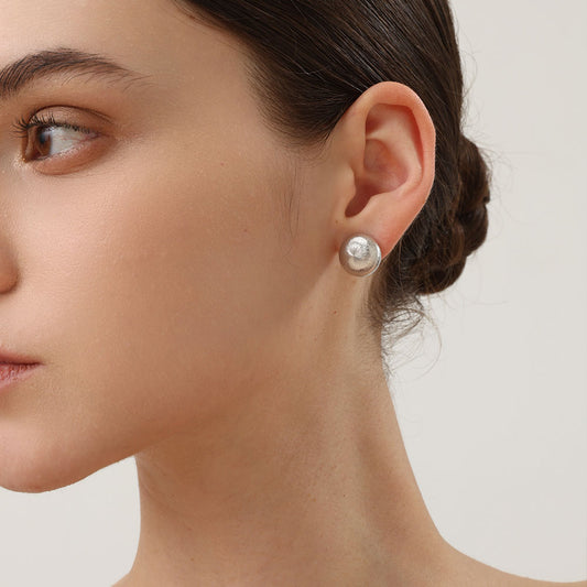 Close-up of a model wearing TIKOO large organic domed stud earrings and matching ring for a modern fashion look.