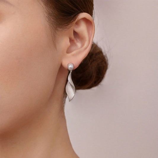 Close-up profile of the sculptural silver-plated twisted leaf dangle earrings on model.