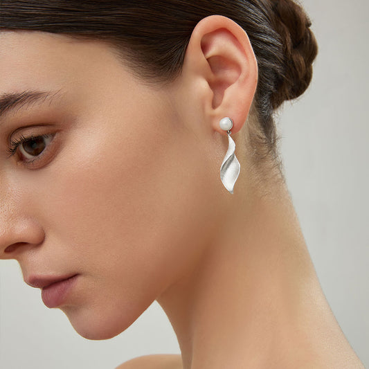 Close-up profile of the sculptural silver-plated twisted leaf dangle earrings on model.