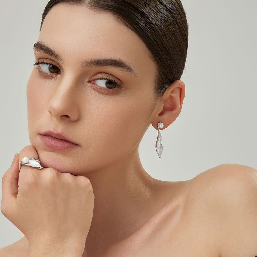 Close-up profile of the sculptural silver-plated twisted leaf dangle earrings on model.