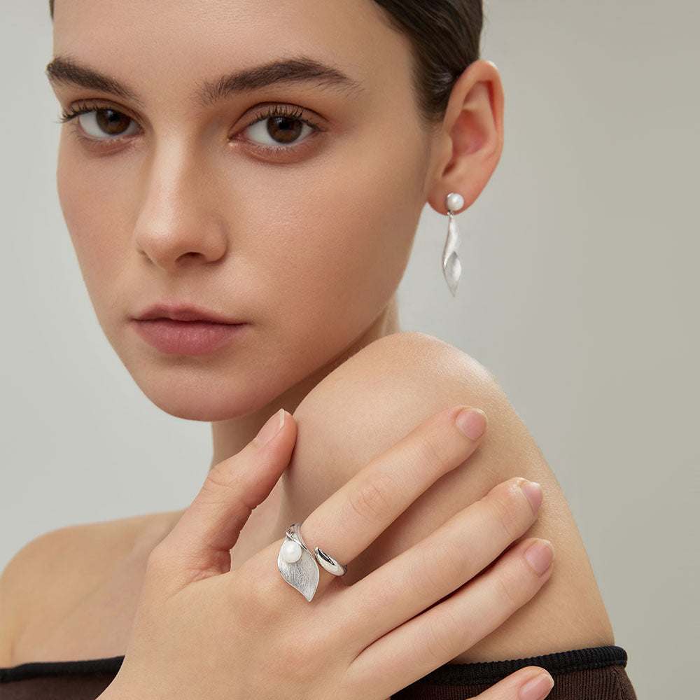 Close-up profile of the sculptural silver-plated twisted leaf dangle earrings on model.