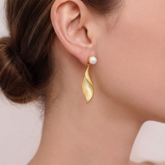 Side profile of a model wearing TIKOO gold leaf dangle earrings with a natural pearl stud.