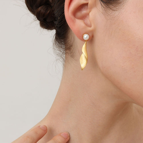Close-up of the textured matte gold leaf earrings on model showcasing the twisted sculptural design.