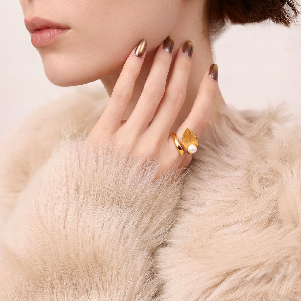 Close-up of a model wearing the TIKOO gold leaf and pearl statement ring with luxury winter fashion.