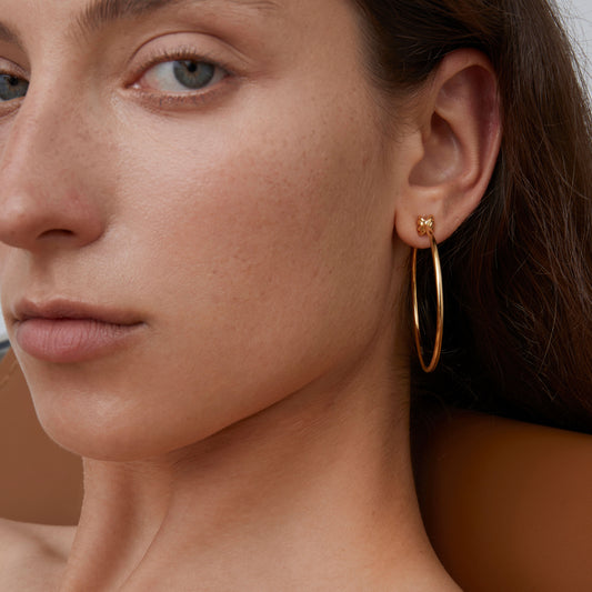 Close-up shot of TIKOO's thick 18K gold-plated large hoops, highlighting the high-shine finish and stud detail.
