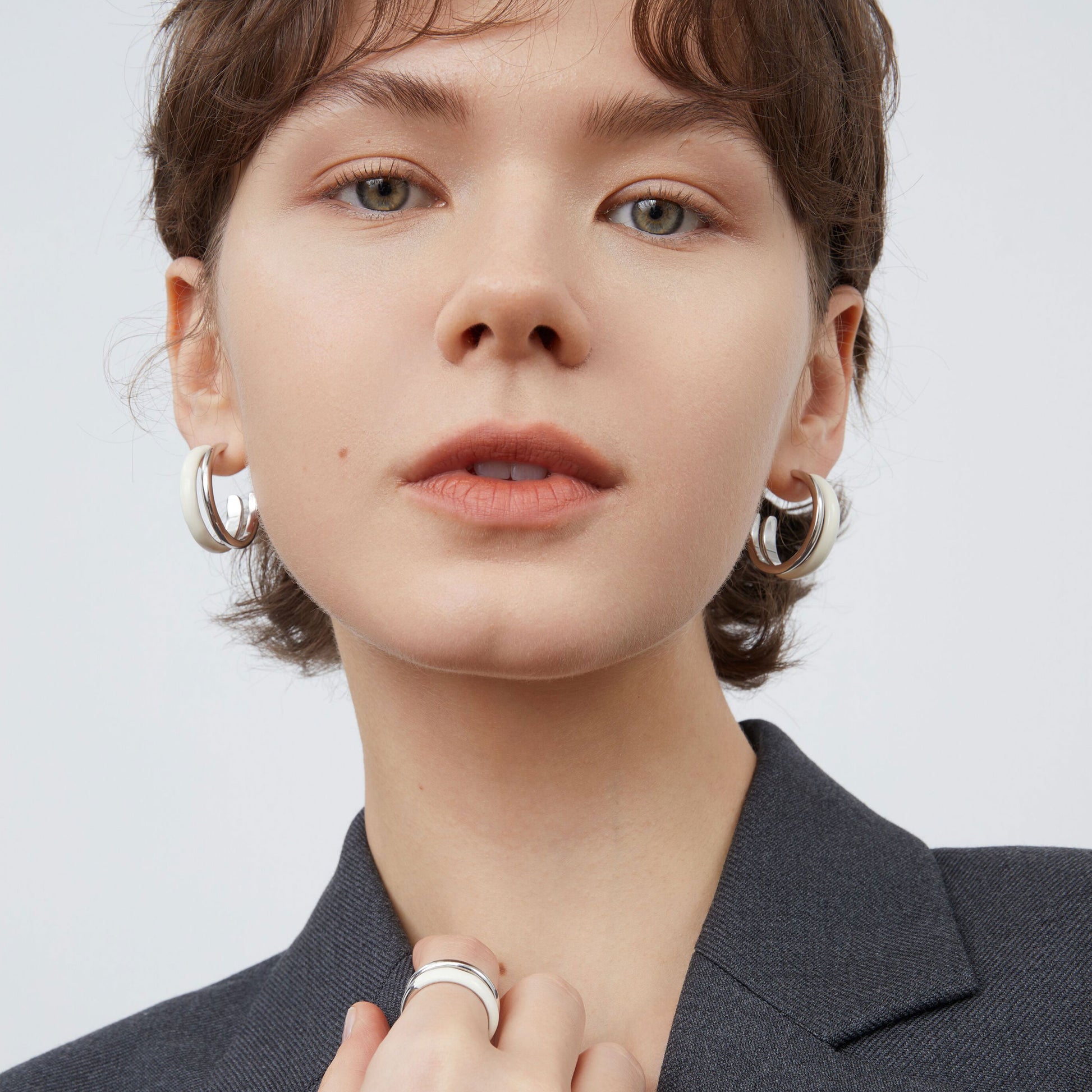 Front view of a model wearing TIKOO minimalist white enamel layered earrings with a black blazer.