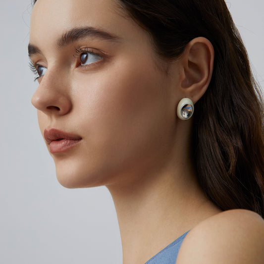 A close-up side profile shot of a model wearing the TIKOO thick platinum plated white enamel hoop earring, highlighting its sculptural design.