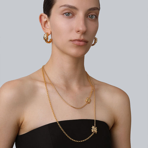 Model showcasing the layered effect of the TIKOO gold knot long necklace paired with matching chunky hoops.
