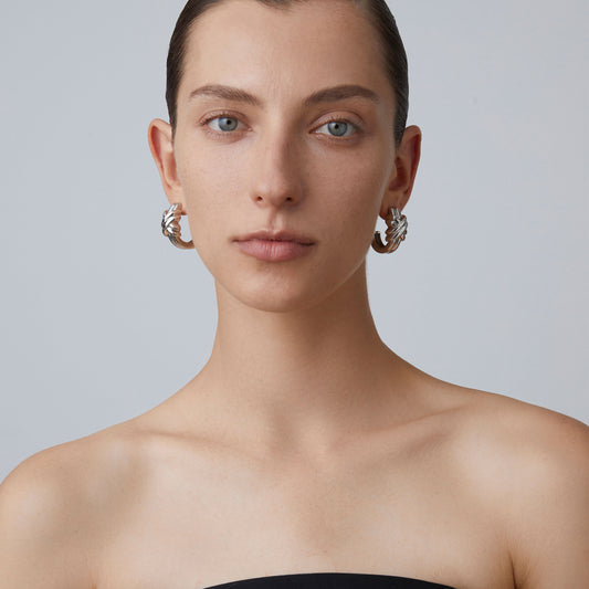 Frontal view of a model wearing TIKOO bold silver-toned knot hoop earrings.