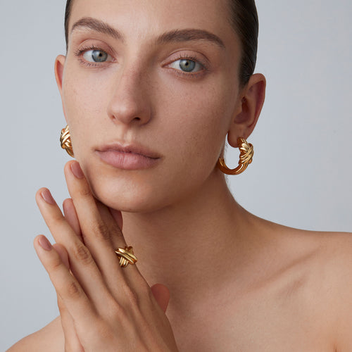 Close-up of the thick 18K gold plated intertwined ring on model's hand, highlighting the sculptural texture.