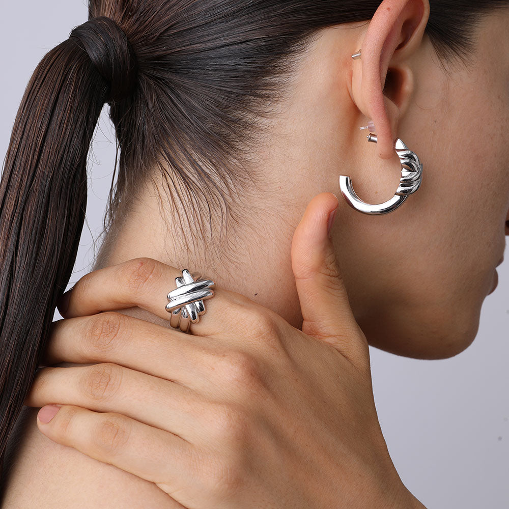 Side view of the thick white gold plated knot ring styled with matching silver hoops.