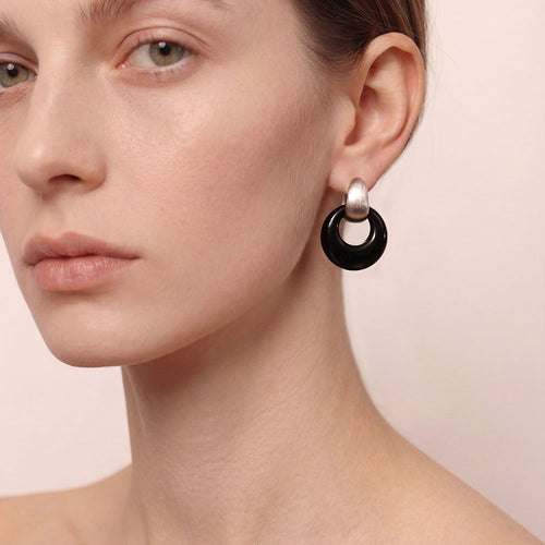 A detailed close-up shot of a model wearing a TIKOO black onyx earring, highlighting the platinum plating and gemstone texture.