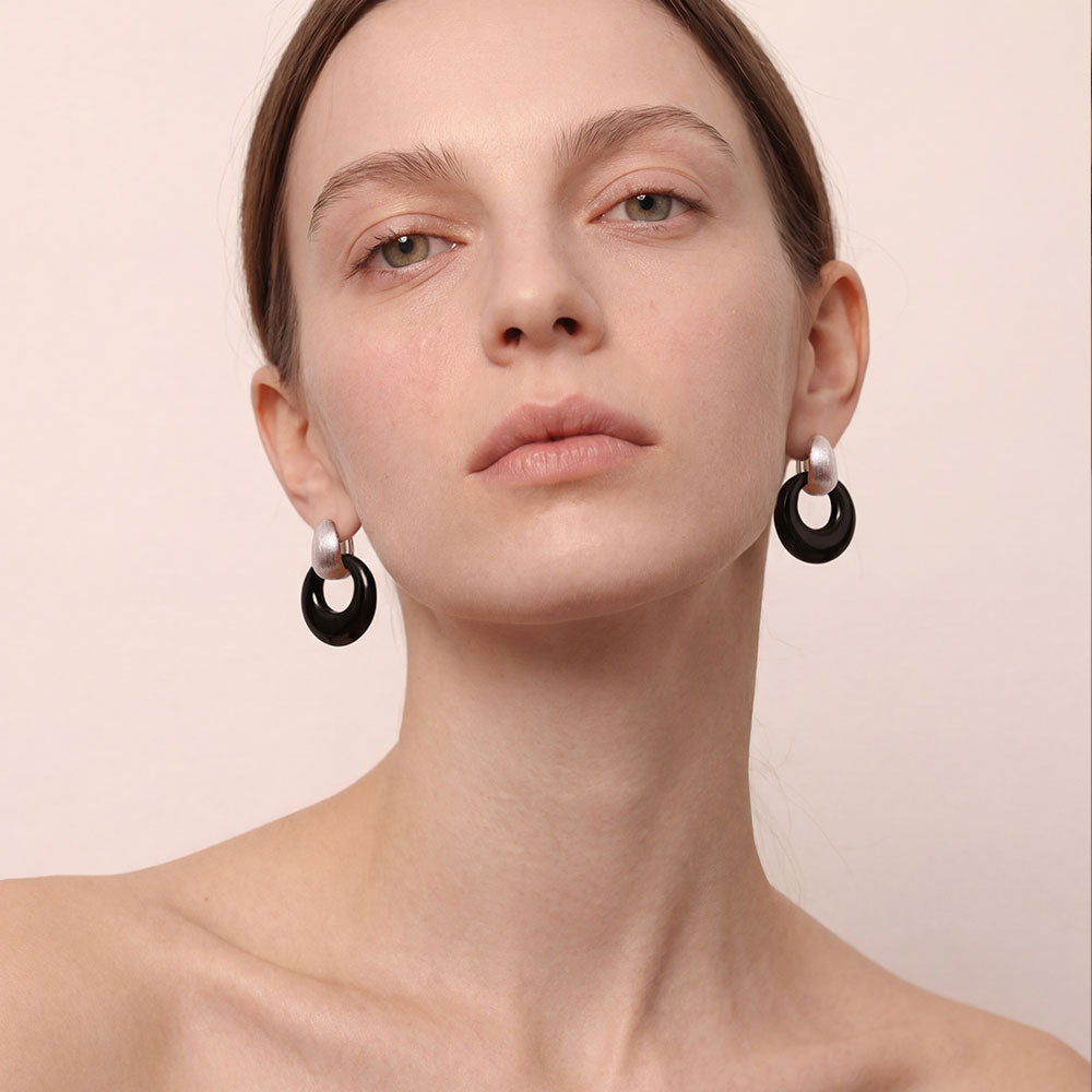 A front view of a model wearing TIKOO's platinum-plated black onyx hoop earrings, showcasing the medium scale and elegance of the design.