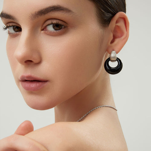 A detailed close-up shot of a model wearing a TIKOO black onyx earring, highlighting the platinum plating and gemstone texture.