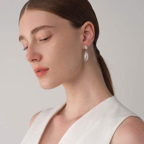 Side profile of a model wearing TIKOO platinum plated earrings, highlighting the texture of the white tiger's eye and leather inlay.