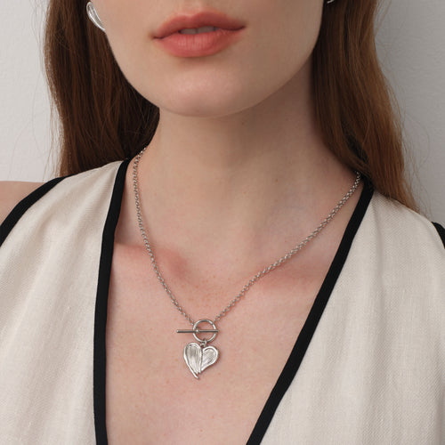 Close up of a model wearing TIKOO heart feather toggle necklace, showing white gold finish and textured details.