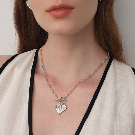 Close up of a model wearing TIKOO heart feather toggle necklace, showing white gold finish and textured details.