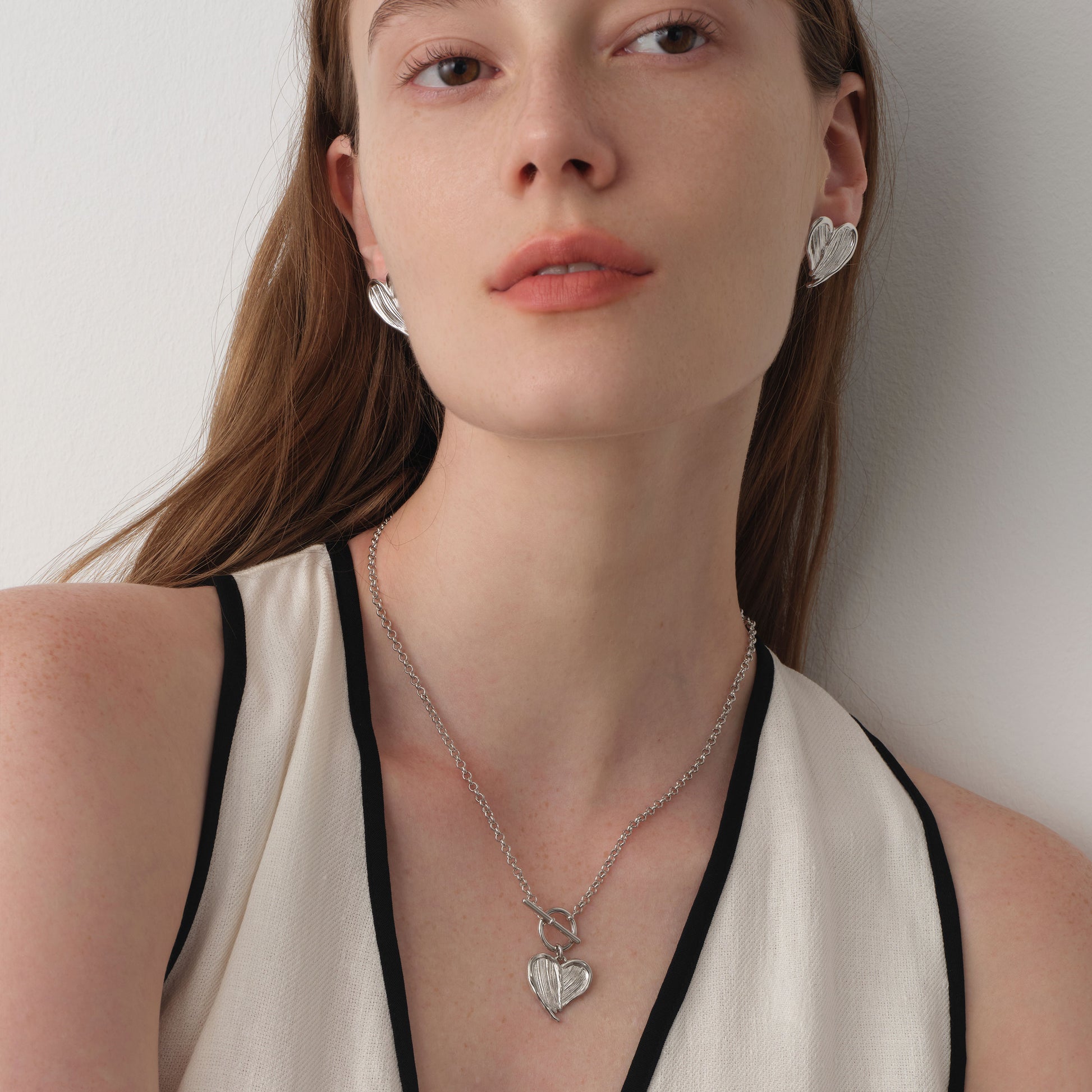 Close up of a model wearing TIKOO heart feather toggle necklace, showing white gold finish and textured details.