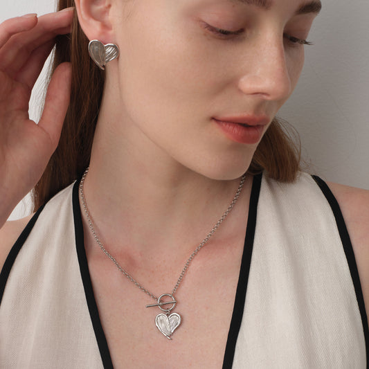 Close up of a model wearing TIKOO heart feather toggle necklace, showing white gold finish and textured details.