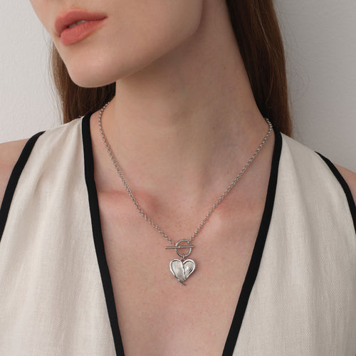 Close up of a model wearing TIKOO heart feather toggle necklace, showing white gold finish and textured details.
