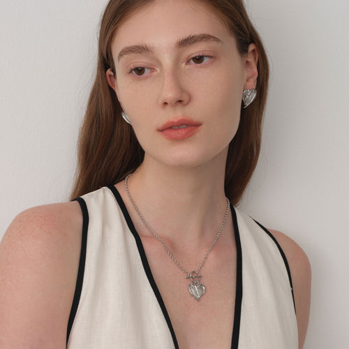 Close up of a model wearing TIKOO heart feather toggle necklace, showing white gold finish and textured details.