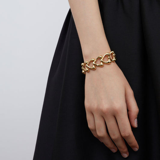 Fashion model styling a chunky gold heart chain bracelet from TIKOO with a black dress.