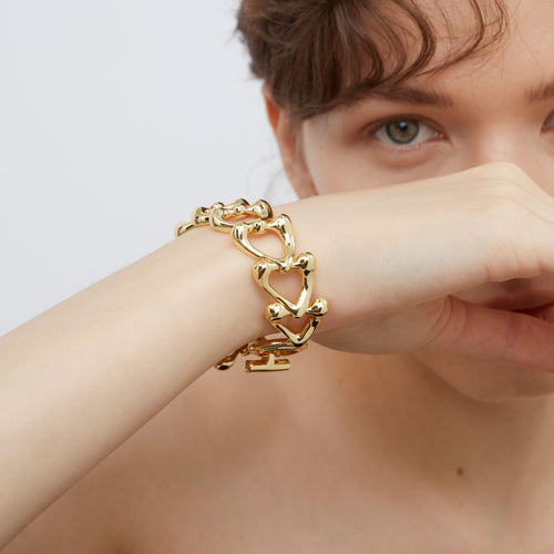 Macro view of the TIKOO 18K gold plated sculptural heart links, highlighting the fluid metal texture and toggle closure.
