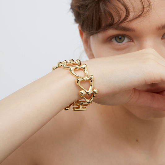 Macro view of the TIKOO 18K gold plated sculptural heart links, highlighting the fluid metal texture and toggle closure.