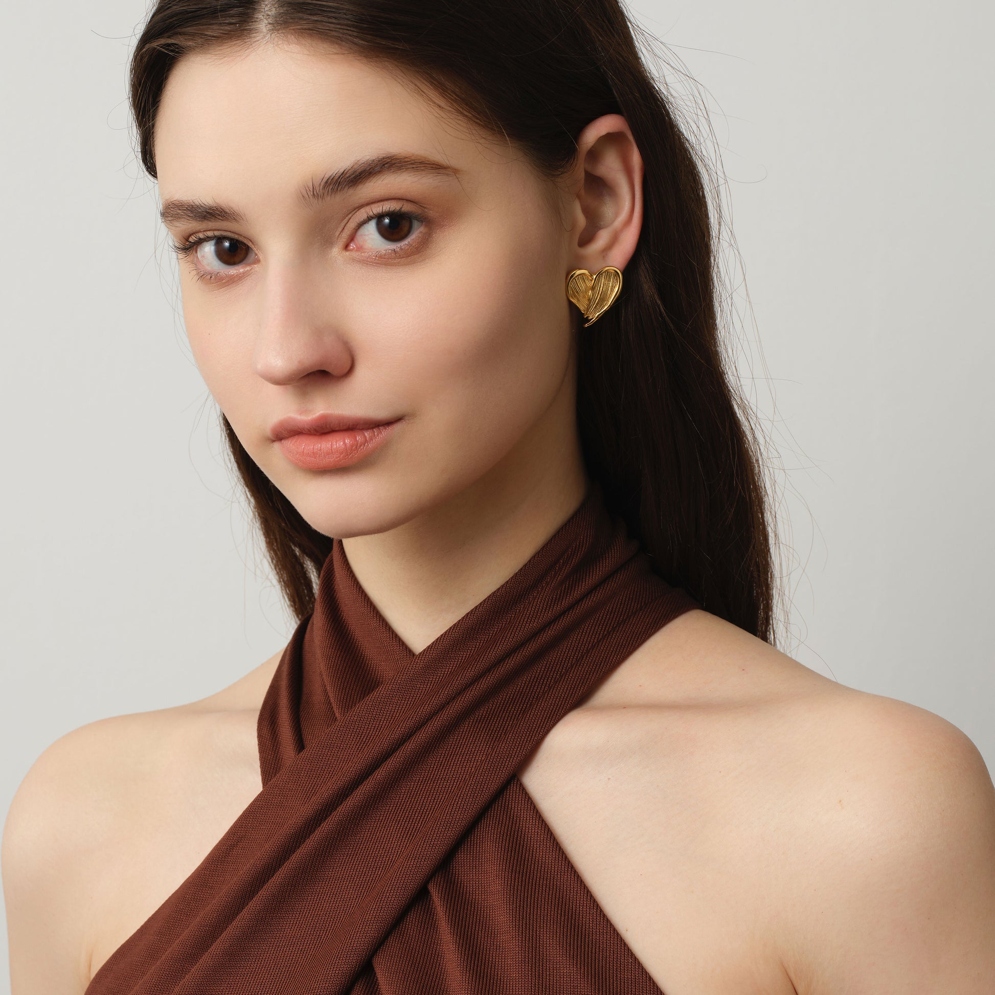 Side profile of a model wearing TIKOO 18K gold plated sculptural heart earrings for a chic look.