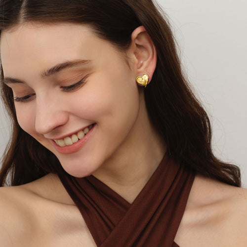 Front view of a model smiling, wearing TIKOO original textured heart studs in rich 18K gold finish.