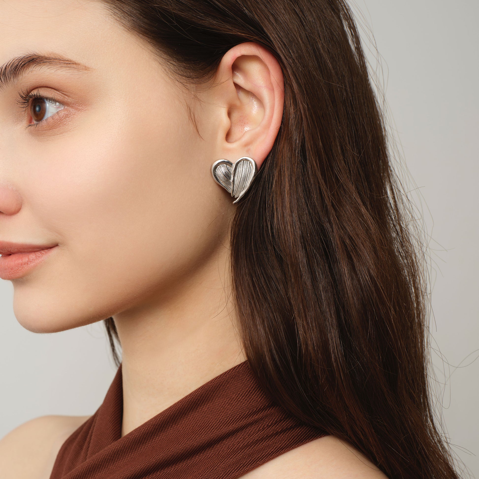 Side view of a model wearing TIKOO white gold heart earrings showcasing the unique linear texture.