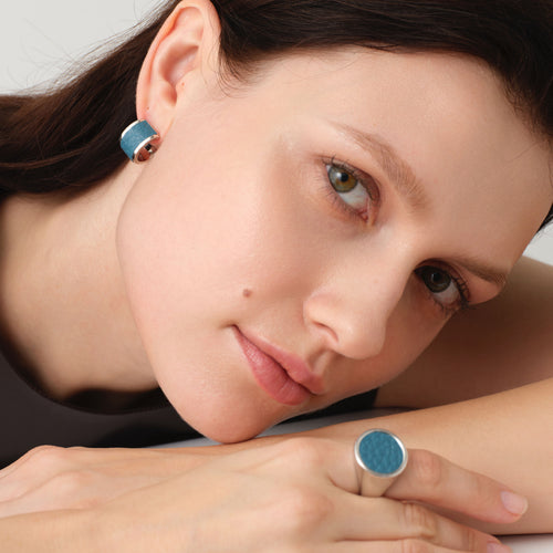 Close-up of model wearing matching TIKOO teal blue leather earrings and signet ring, showcasing the textured leather jewelry set.