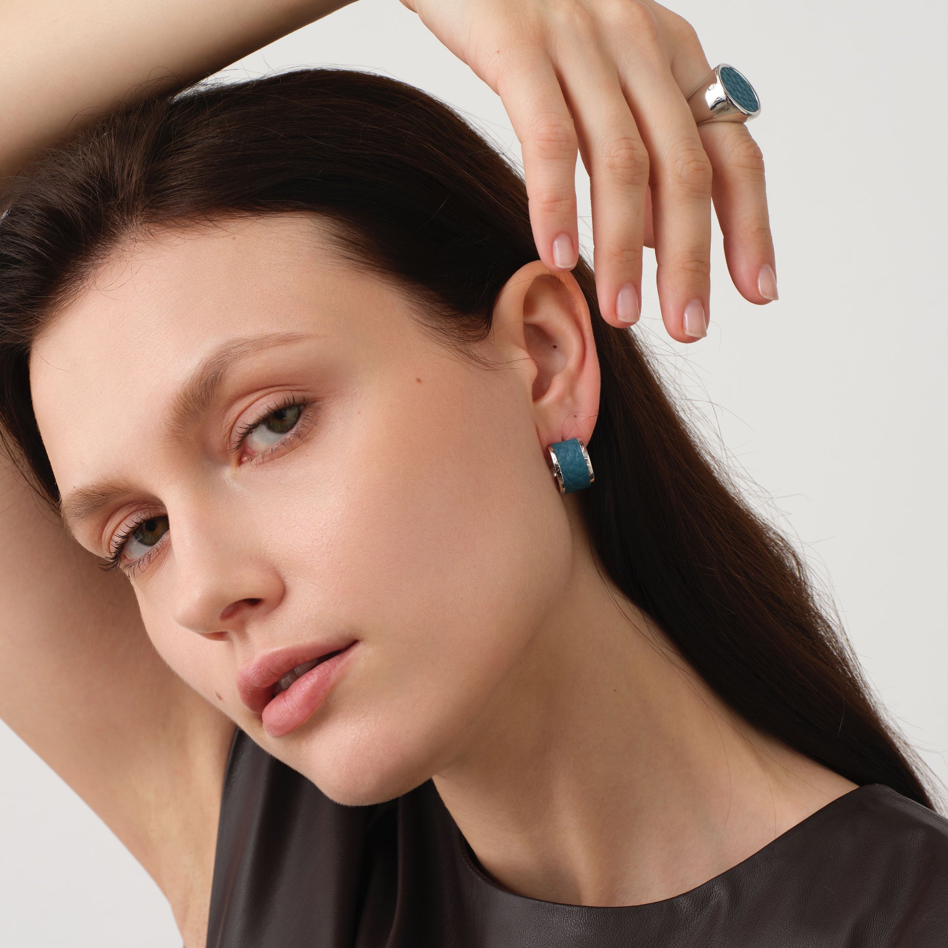 Close-up of a model wearing TIKOO teal blue leather earrings and matching ring, showcasing the textured leather and white gold finish.