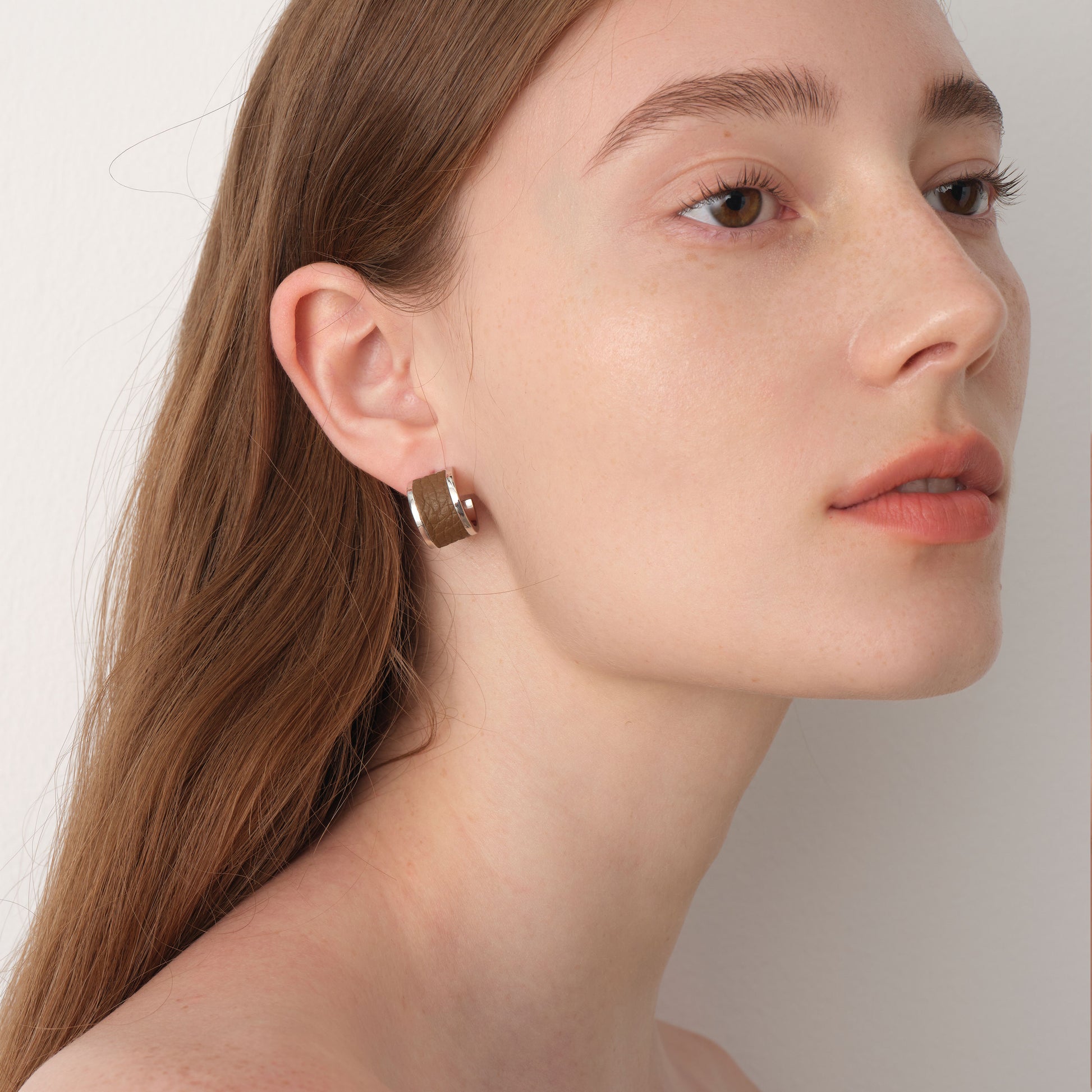 Fashion model wearing TIKOO brown leather inlay earrings, showcasing a minimalist and elegant jewelry look.