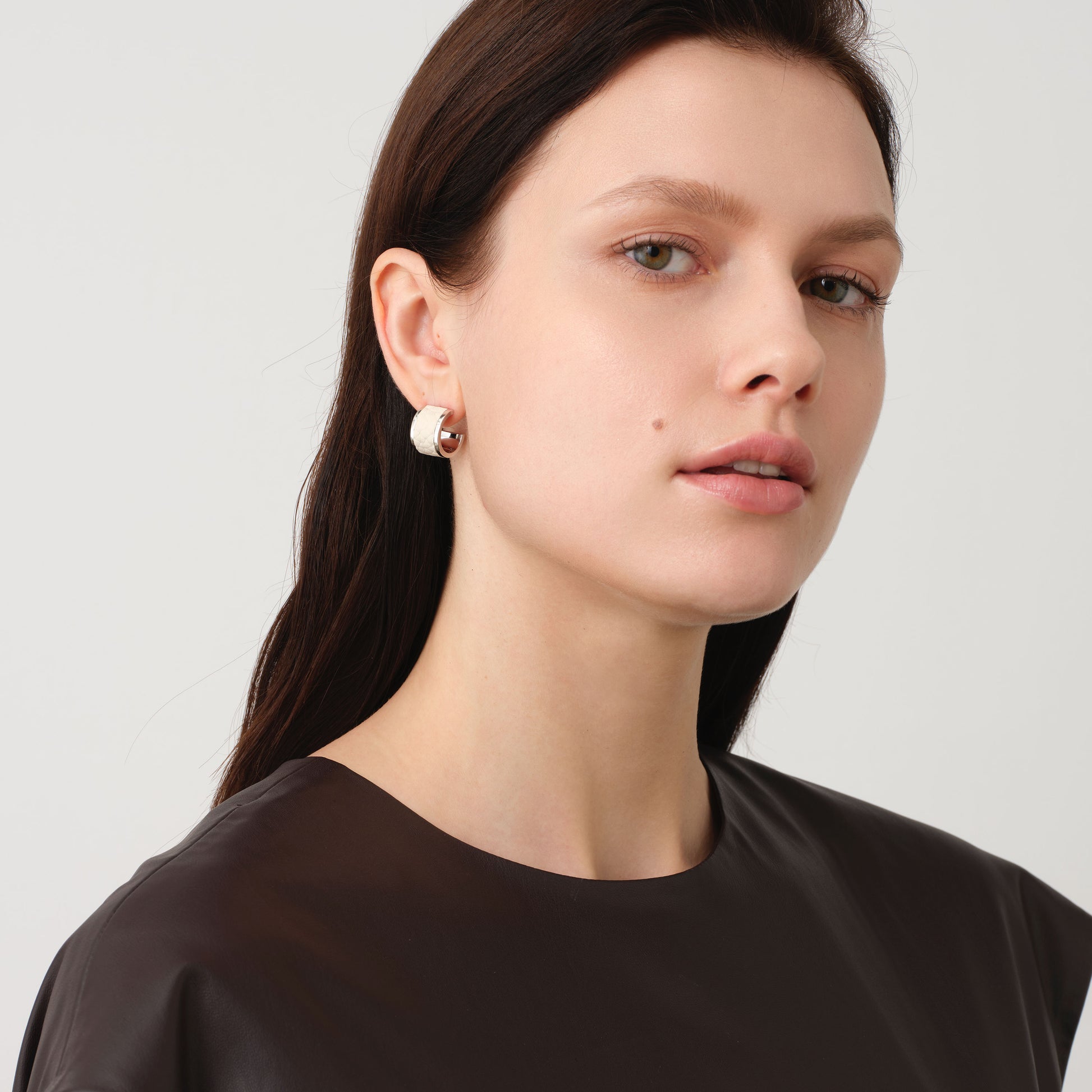 Professional model showcasing TIKOO leather inlay earrings, highlighting the contrast between the white leather and polished white gold finish.