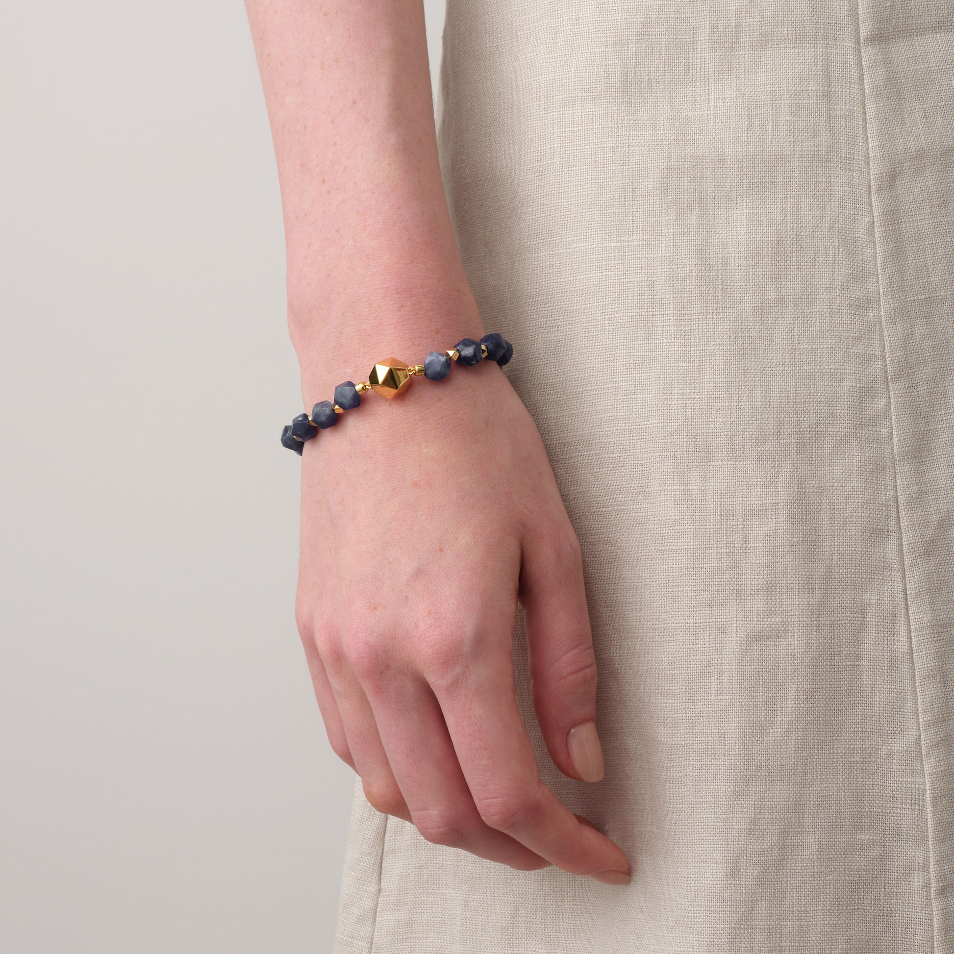 Close-up of model's wrist wearing TIKOO blue sodalite gemstone bracelet with a neutral linen dress.
