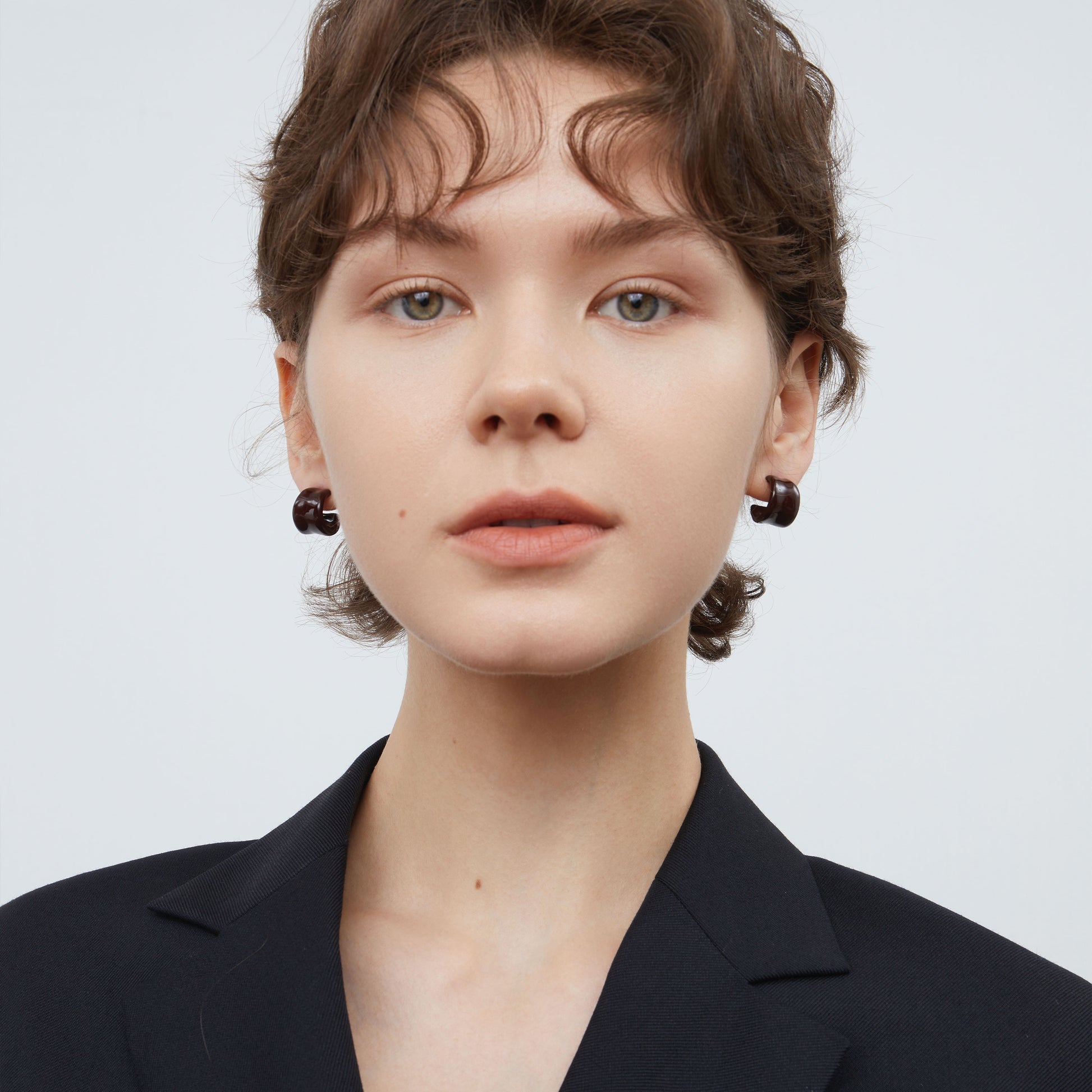 Front view of a model wearing TIKOO espresso brown enamel hoop earrings with a black blazer.
