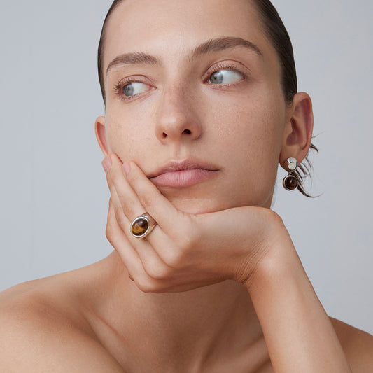 Fashion model showcasing a bold TIKOO tiger's eye silver ring and matching earrings.