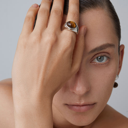 Close-up of a minimalist 925 silver statement ring with a brown tiger's eye gemstone on model's finger.