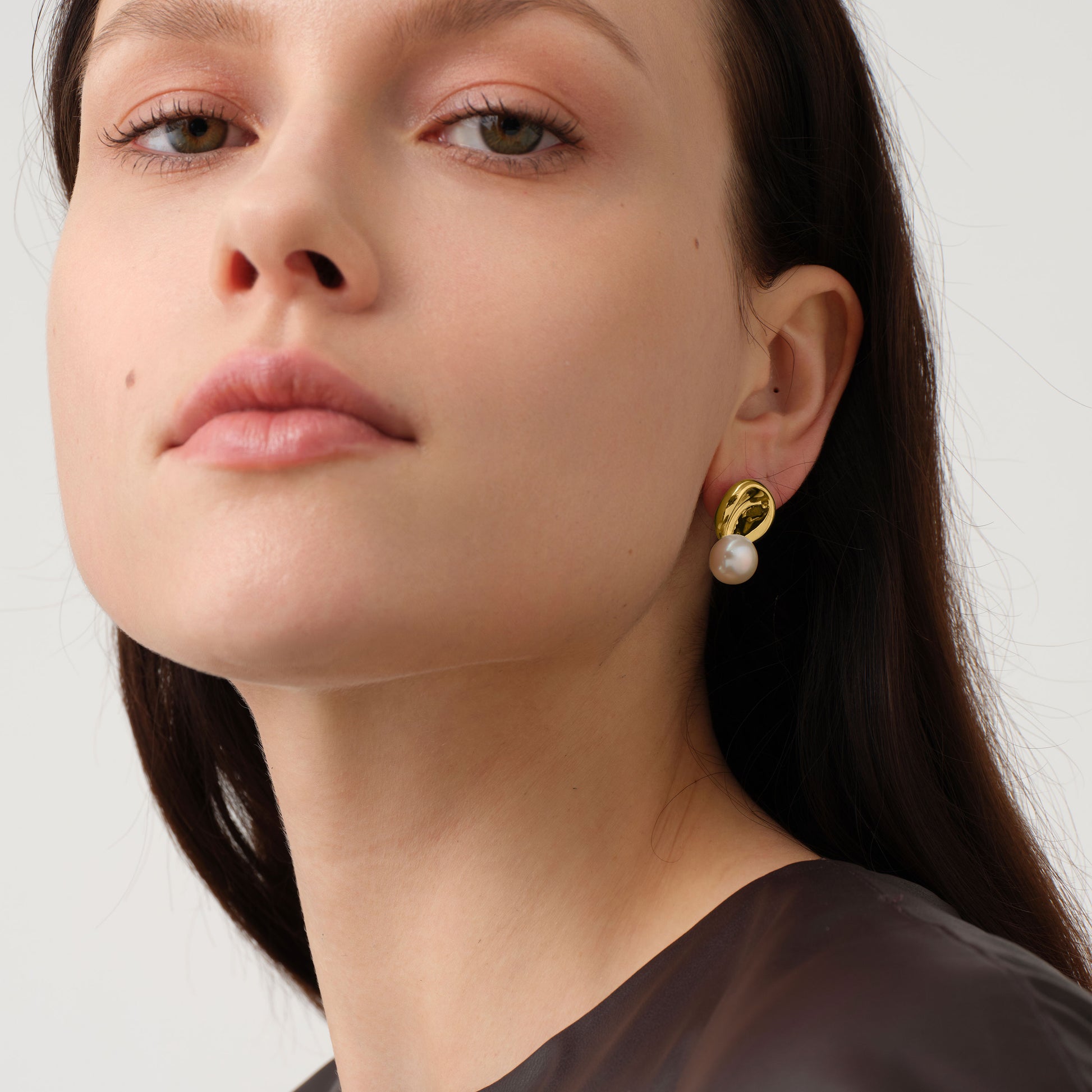 Close up of a model wearing TIKOO original designer pearl earrings with thick 18K gold plating.