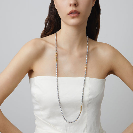 Fashion model wearing TIKOO long grey Swarovski pearl necklace, full length drape, styled with a white strapless top.