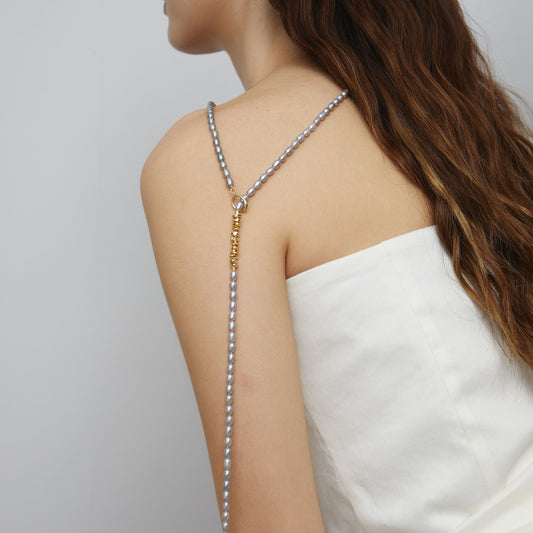 Close-up of model styling TIKOO grey Swarovski pearl necklace as a Y-shaped lariat with 18K gold toggle clasp visible.