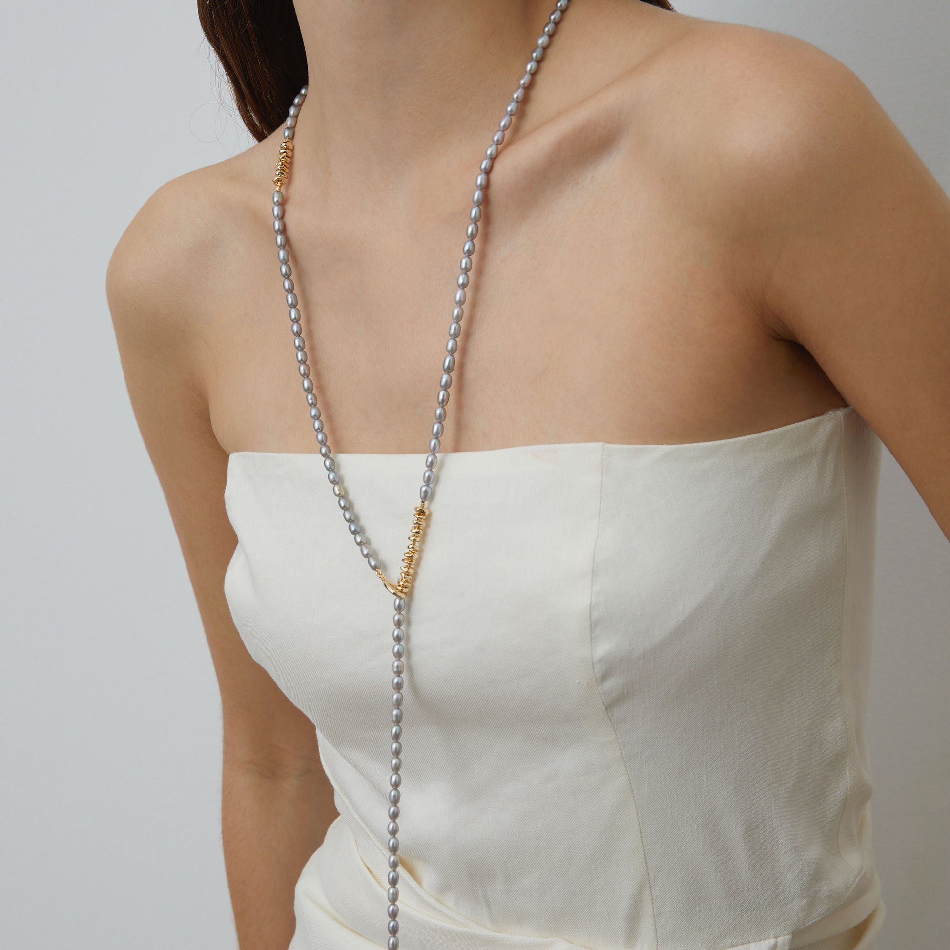 Close-up of model styling TIKOO grey Swarovski pearl necklace as a Y-shaped lariat with 18K gold toggle clasp visible.