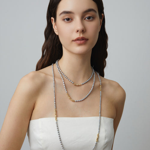 High-fashion close-up of model wearing TIKOO grey Swarovski pearl necklace as a double-strand choker, showing rich gold plating detail.